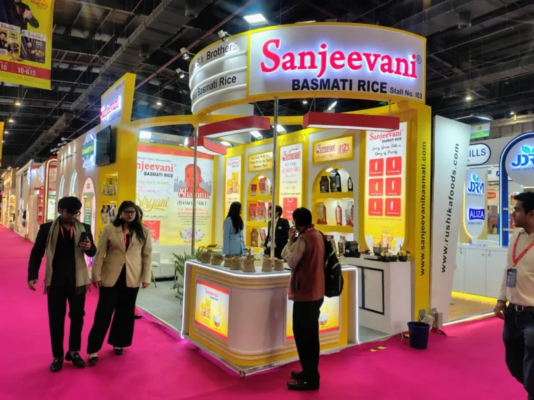 Trade show booth for Sanjeevani Basmati Rice with bright yellow and white design, product displays, and visitors walking around.
